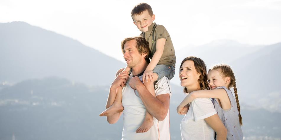 A happy family with two children enjoys the mountain view – the parents carry the children on their shoulders.